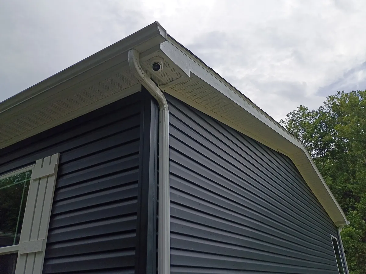 Dome security camera mounted under the eave of a home with dark navy vinyl siding