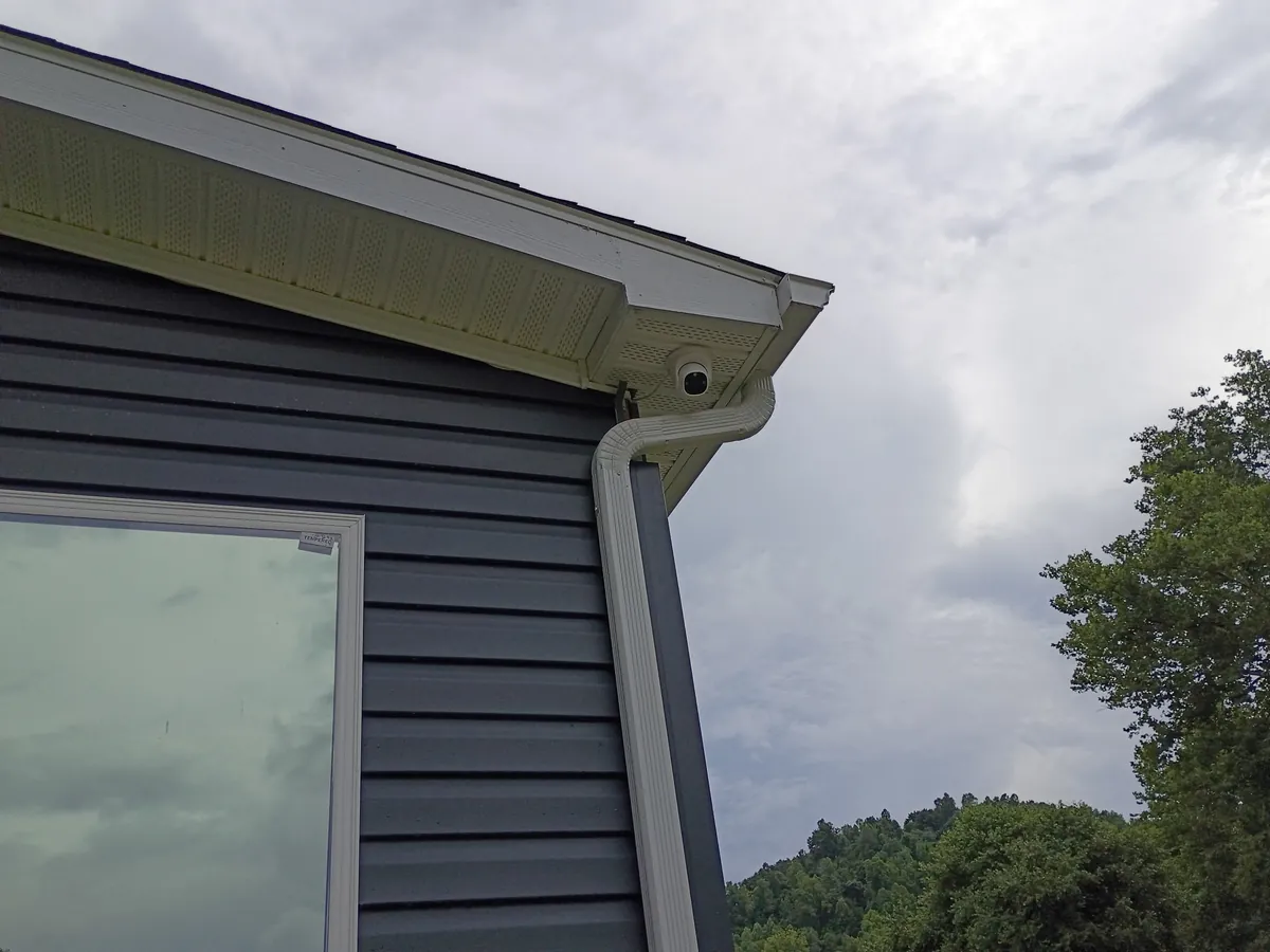 White dome security camera installed at the roofline of a home beside the downspout