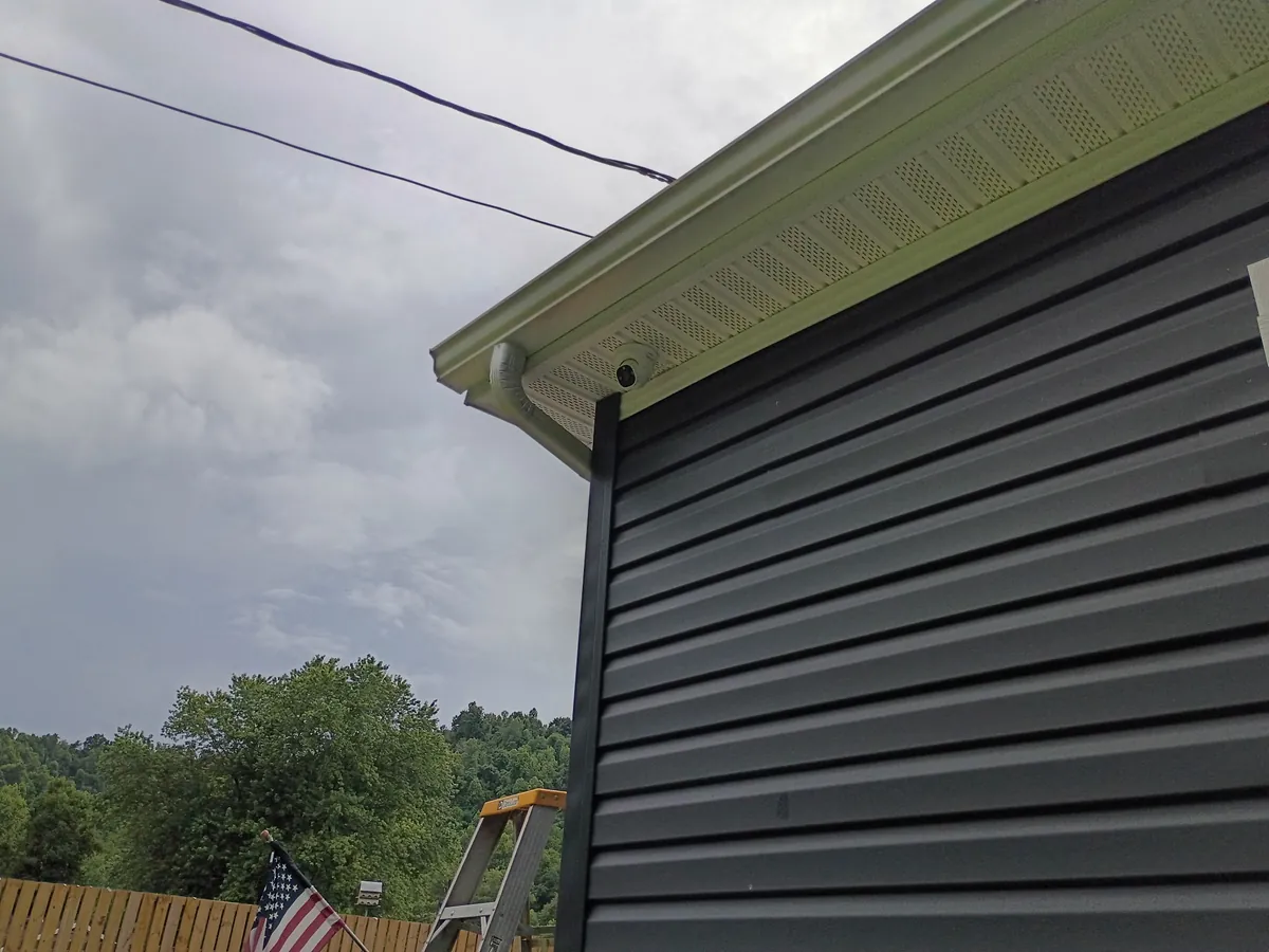 Dome security camera installed under the eave of a dark-sided home